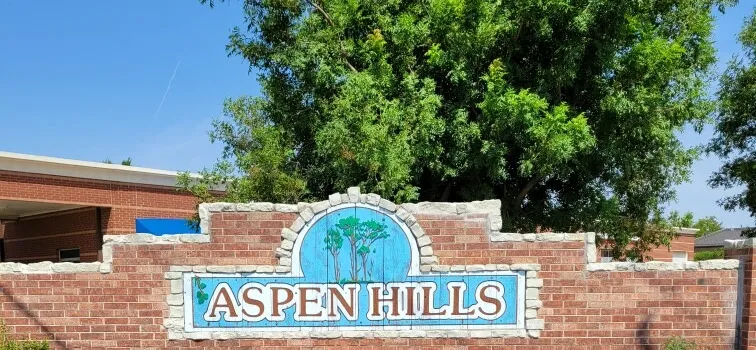 Picture of the Aspen Hills Neighborhood entrance sign. A tree is behind it.